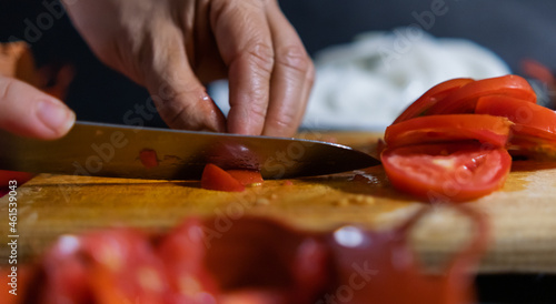 Hands slicing tomato on a wooden cutting board