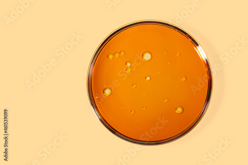 Top view of petri dish with cosmetic oil inside.Yellow background with copy space.