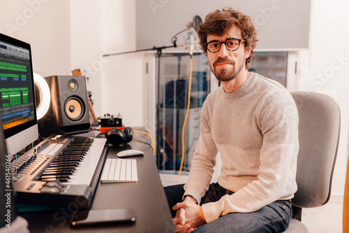 Male music producer working with his computer at home music studio. Millennial musician looking at camera. photo