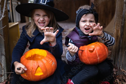 Little girls make jack-o-lantern from big pumpkins for celebratiion of halloween holiday.Witch costume, hat, coat. Cut with knife,take out pulp with seeds.Outdoors activity, backyard.Children's party photo