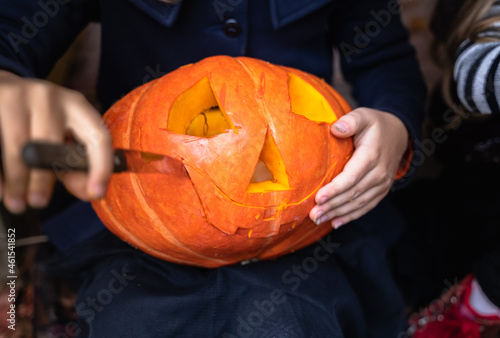 Little girls make jack-o-lantern from big pumpkins for celebratiion of halloween holiday.Witch costume, hat, coat. Cut with knife,take out pulp with seeds.Outdoors activity, backyard.Children's party photo