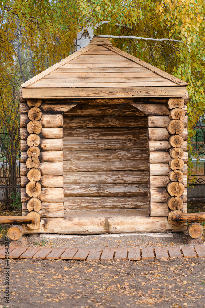 Gazebo made of logs with a wooden bench next to it, vertical photo