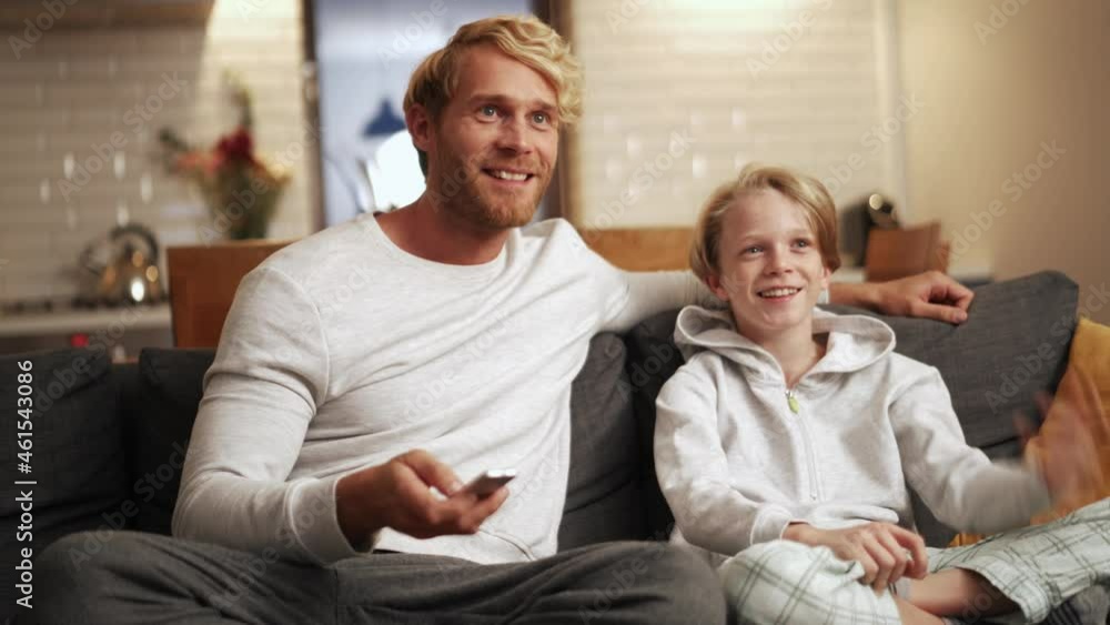 Smiling father and son watching tv and talking on the couch Smiling father and son watching tv and talking on the couch