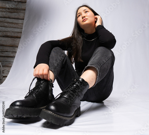 portrait of a girl in black clothes with long black hair on a gray background. Eastern beauty. sitting on the floor. shot from the bottom with a wide-angle lens