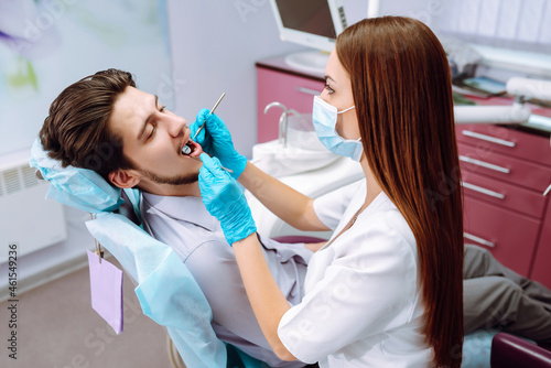 Young man at the dentist's chair during a dental procedure. Overview of dental caries prevention. Dentist examining patient's teeth in modern clinic. Healthy teeth and medicine concept.
