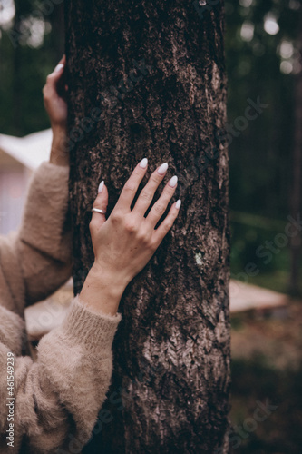 the girl's hands in a brown sweater with white nails touch the tree trunk