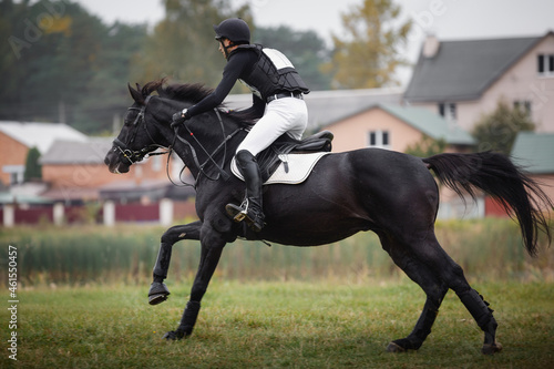 portrait of rider man and black stallion horse galloping during eventing cross country competition in autumn