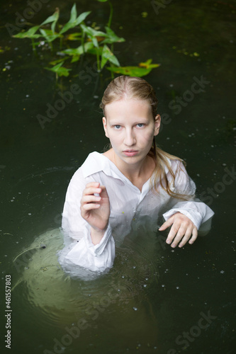 Young nymph woman in the green pond with water lilies