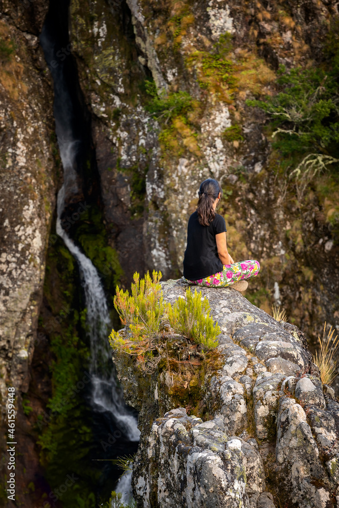 Woman relaxing looking at a waterfall sitting on a rock landscape in Geres national park, in Portugal