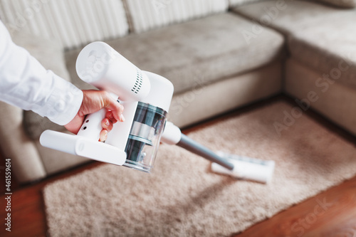 Fotografi Powerful cordless vacuum cleaner with white cyclonic dust collection technology in hand, cleans the carpet in the house near the sofa