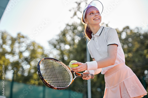 Positive female tennis player holding racket and ball in hands going to throw to opposer while training workout before competition, on hardcourt. Wellbeing, sport, healthy lifestyle concept