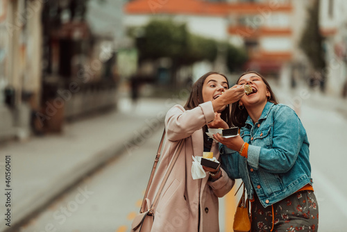 Two woman walking around modern town and eating fresh poffertjes. Selective focus