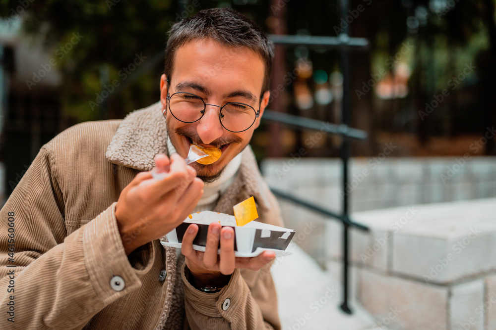 Fototapeta premium A modern guy who wears glasses, sitting in the park and eats fresh poffertjes