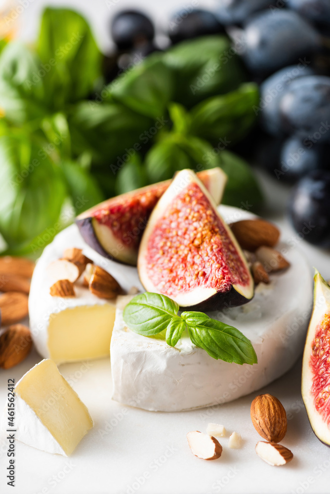 Camembert cheese with figs, grapes, nuts and basil on white marble background, closeup view