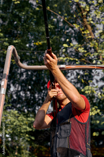 confident man aiming with hunting rifle in the outer wood. Carbine with optical-sight. Caucasian young guy in protective headphones, eyeglasses in uniform is concentrated on shooting. view from below