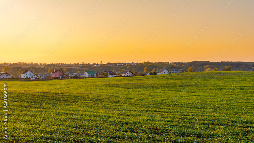Green agricultural field, holiday village on the horizon. Orange sky after sunset. Autumn Nature