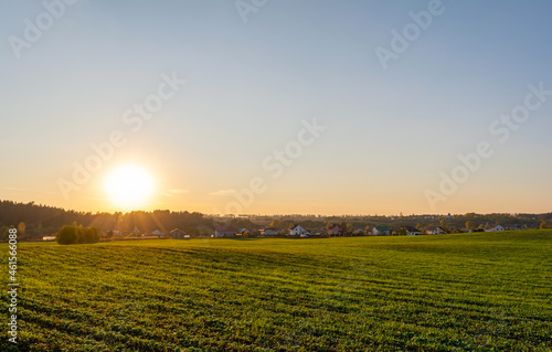 Green agricultural field, holiday village on the horizon. Blue orange sky during sunset. Autumn Nature