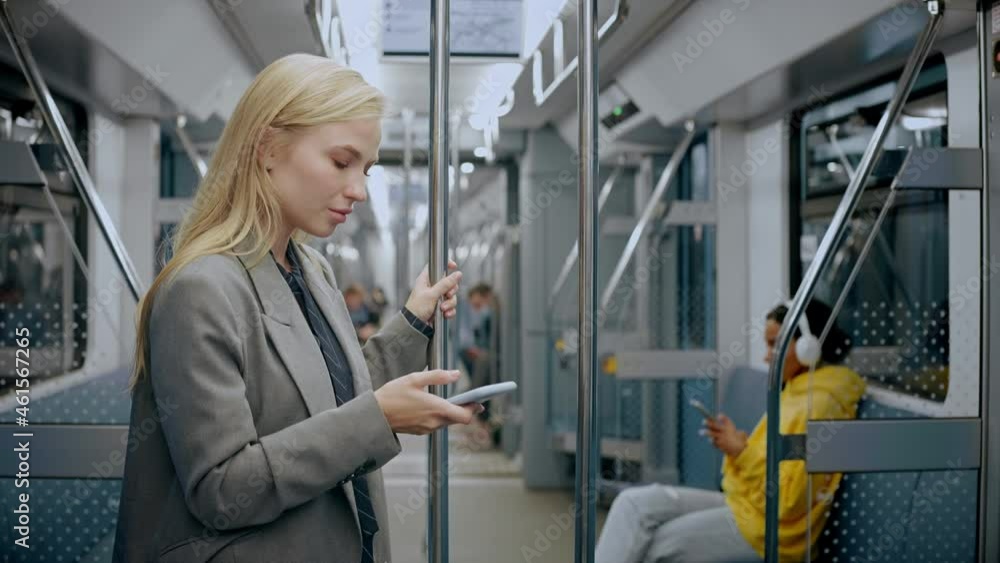 Young blonde girl standing in modern metro train and looking at her phone and texting. She is wearing a business suit, looking tired after work. High quality 4k footage Young blonde girl standing in modern metro train and looking at her phone and texting. She is wearing a business suit, looking tired after work. High quality 4k footage