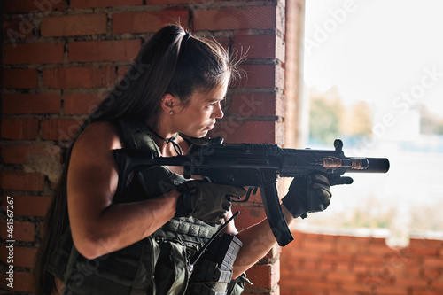 Wallpaper Mural Side view on young adult woman with sniper rifle with telescopic sight, fit lady keep the defense in battle and aims at enemy. Abandoned brickwall building with windows . Military forces, army Torontodigital.ca
