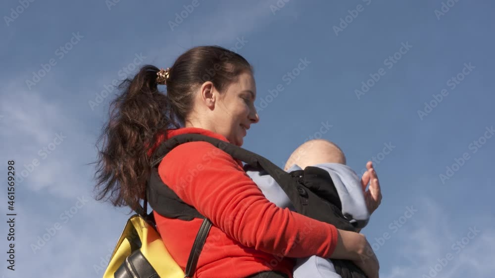 Happy family against the sky, mom and child on a sunny summer day, mother with son in baby carrier on a walk outdoors. High quality 4k footage. High quality 4k footage Happy family against the sky, mom and child on a sunny summer day, mother with son in baby carrier on a walk outdoors. High quality 4k footage. High quality 4k footage