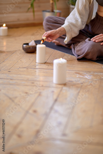 close-up woman Burning palo santo for home purification and meditation, sitting on mat on floor, alone. in domestic cozy atmosphere at day time. close-up hands of yoga practitioner