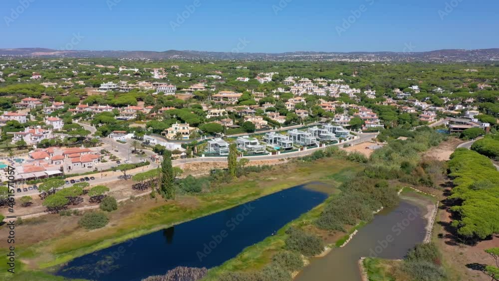 Aerial overview of Quinta do Lago resort buildings in Vale de Lobo, Algarve, Portugal, Europe. Shot of rooftops of luxury cottages in green landscape with mountains on background. Golf fields. Aerial overview of Quinta do Lago resort buildings in Vale de Lobo, Algarve, Portugal, Europe. Shot of rooftops of luxury cottages in green landscape with mountains on background. Golf fields.