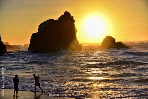 Portugalia. Plaża, Praia da Ursa z sylwetkami fotografujących się chłopców na tle zachodzącego nad oceanem słońca i skał. © polmus