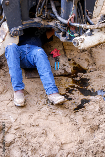 Mechanic working underneath a backhoe leaking oil