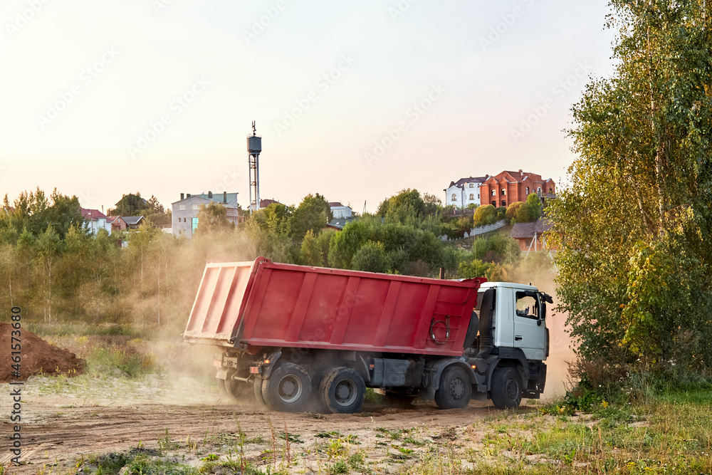 Fototapeta premium Red dump truck simultaneously lifted the bodies to unload the sand. Cargo transportation services. Large multi-ton truck. Unloading cargo. Construction site and machinery. Banner. Common view