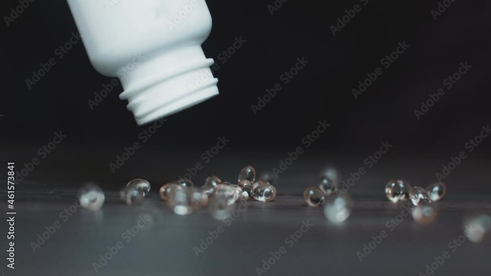 A lot of pills in gelatin capsules dropped on the dark surface from the white plastic bottle for drugs. Conceptual footage about medical drugs abuse and harmful addiction. A lot of pills in gelatin capsules dropped on the dark surface from the white plastic bottle for drugs. Conceptual footage about medical drugs abuse and harmful addiction.