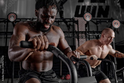 Men exercise bike gym cycling training fitness. Two Fitness male using air bike cardio workout. Two guys biking indoor at gym, exercising legs. Cross functional training. focus on black male