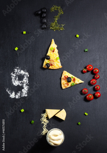 Pizza time, pizza ingredients and pizza in the shape of a clock drawn on a chalk board: cheese, seasonings, basil, onion, water, flour, olives, tomatoes