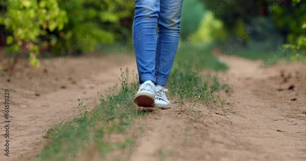 Close-up, women's legs in white sneakers are walking along a path in the forest. Slender legs in jeans are walking along a sandy path, a walk in the forest. Bottom view. 4k, ProRes Close-up, women's legs in white sneakers are walking along a path in the forest. Slender legs in jeans are walking along a sandy path, a walk in the forest. Bottom view. 4k, ProRes