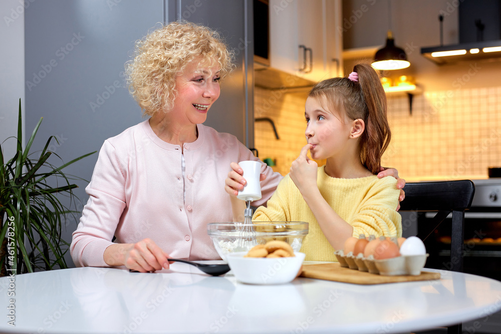 Happy loving caucasian family preparing bakery together. Mature Granny and pretty child are cooking cookies and having fun in cozy kitchen at home. Homemade food and little helper, making dough Happy loving caucasian family preparing bakery together. Mature Granny and pretty child are cooking cookies and having fun in cozy kitchen at home. Homemade food and little helper, making dough