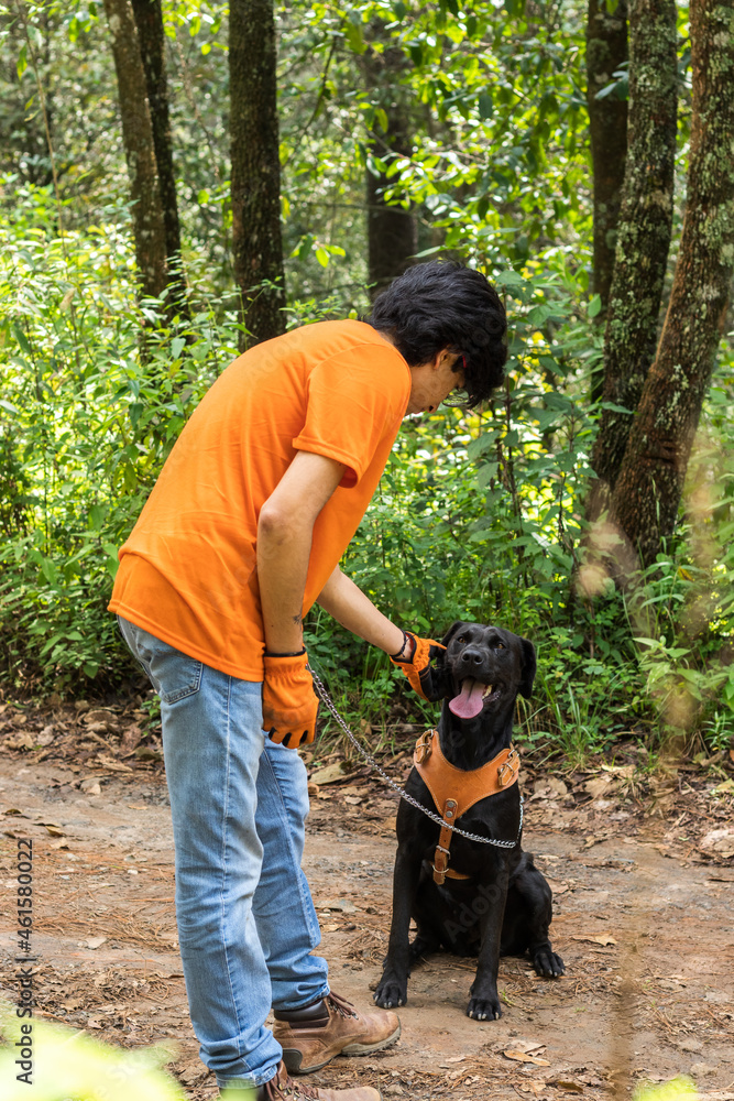 young man wearing an orange t-shirt, petting his dog in the forest young man wearing an orange t-shirt, petting his dog in the forest