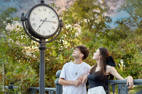young guy and a girl are looking at a large clock installed on the street