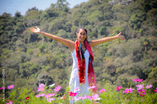 Carefree young woman standing in a field of flowers with mountains in the background