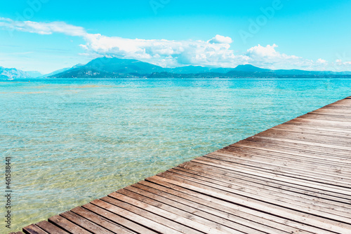 Planked wooden walkway over a tranquil lake with high mountains in the background in a tranquil scene at Lago di Garda.