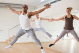 Positive Hispanic man jumping while dancing synchronous group choreography in modern dance studio