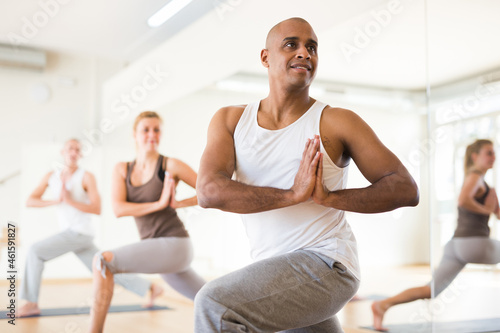 Positive man practicing yoga lesson at group class, maintaining healthy lifestyle photo