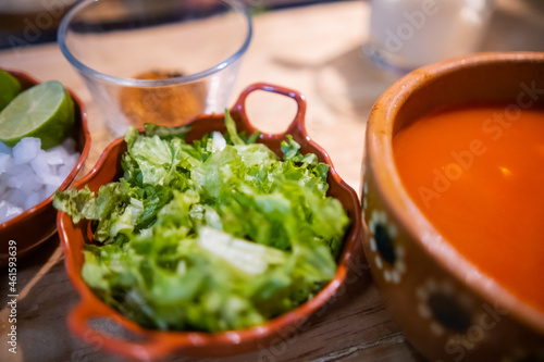 Clay bowls of chopped vegetables and delicious traditional Mexican pozole