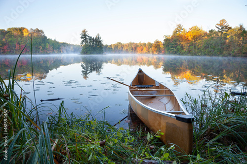 Yellow canoe on shore of calm lake with island at sunrise during autumn