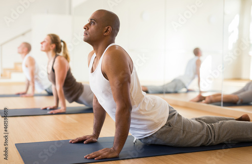 Young adult man exercising yoga with group of sporty people in studio