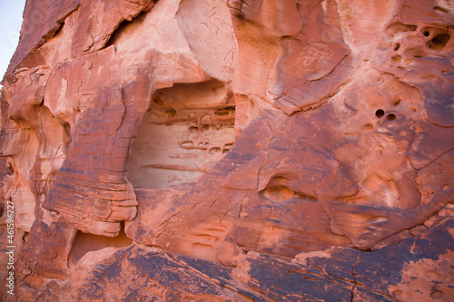 closeup of red sandstone face of rock formation with windblown holes and petroglyphs