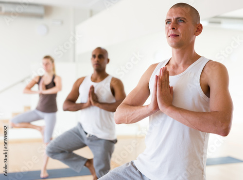 Portrait of young adult man making yoga exercises with group at fitness center