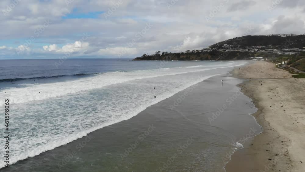 A drone flies over crashing ocean waves at the beach as surfers paddle out to surf. A drone flies over crashing ocean waves at the beach as surfers paddle out to surf.