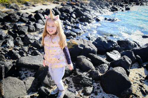 Cute little girl wearing unicorn headband walking along rocky beach © Caseyjadew
