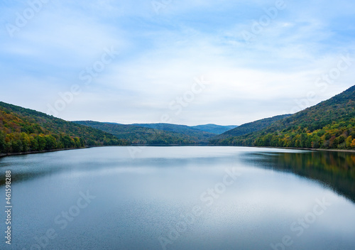 Pepacton Reservoir, Catskills, NY. Beautiful calm lake surrounded by forest. Colors of the leaves starting to change with the fall season, and reflections in the water. Blue sky, copy space. 