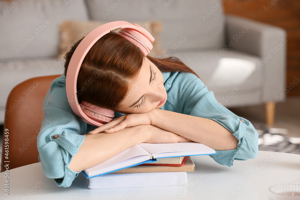 Tired young woman with headphones and books sleeping at table Tired young woman with headphones and books sleeping at table