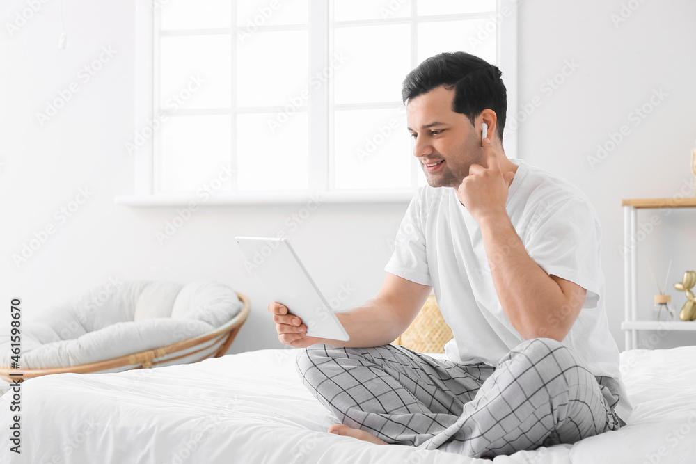 Young man with tablet computer and earphones in bedroom Young man with tablet computer and earphones in bedroom